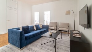 Ein modernes Wohnzimmer mit einem blauen Sofa, einem Couchtisch und zwei Sesseln. An der Wand ist ein Flachbildfernseher angebracht.