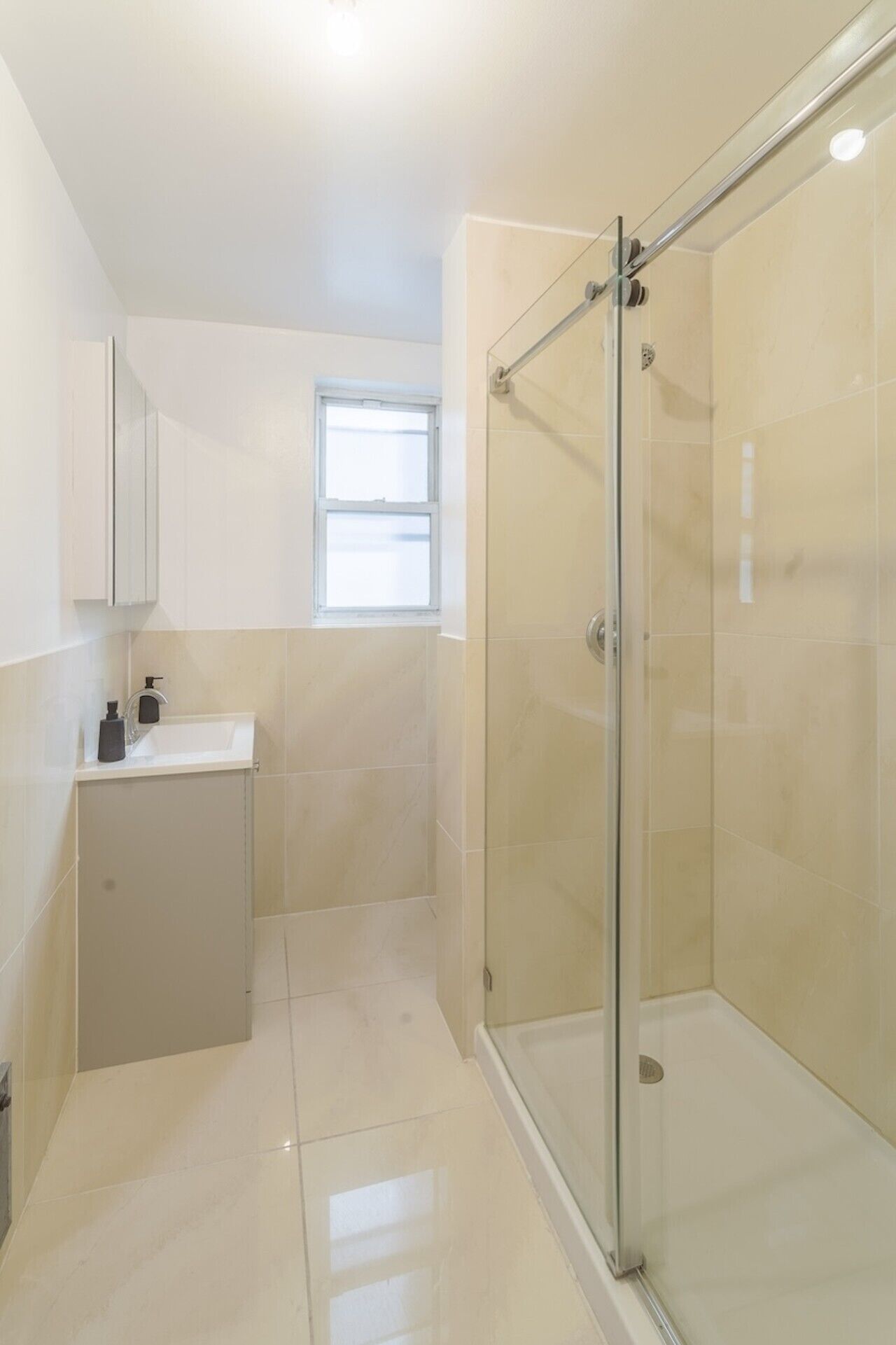 A modern bathroom with a glass-enclosed shower, a sink with a soap dispenser, and a window providing natural light.