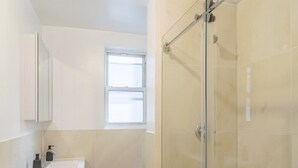 Ein modernes Badezimmer mit einer gläsernen Duschkabine, einem Waschbecken mit Seifenspender und einem Fenster für natürliches Licht.