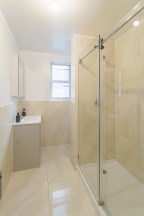 Ein modernes Badezimmer mit einer gläsernen Duschkabine, einem Waschbecken mit Seifenspender und einem Fenster für natürliches Licht.