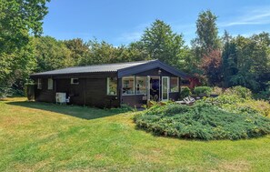 Eine kleine Holzhütte mit einer Veranda, umgeben von einem gepflegten Garten und Bäumen.