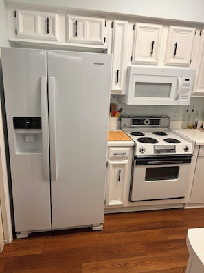 A kitchen with white cabinetry, a Whirlpool refrigerator, a microwave, and a stove.
