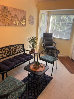 A living room with a sofa, two chairs, a coffee table, a potted plant, and a window with blinds.