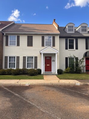 A two-story residential building with a red front door, white siding, and a small front yard.