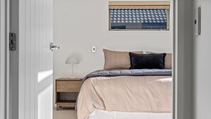 Ein Schlafzimmer mit Bett, Nachttisch, Lampe und einem Fenster mit Jalousien.