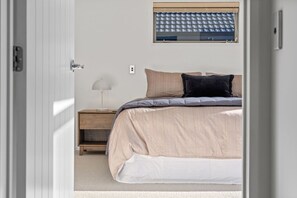 Ein Schlafzimmer mit Bett, Nachttisch, Lampe und einem Fenster mit Jalousien.