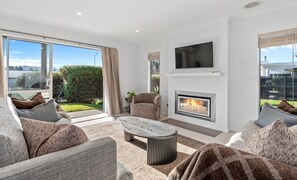 A modern living room with a fireplace, comfortable seating, and large windows. - Family Ski Base | Boot Dryer | 4Bedroom (Wānaka)
