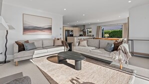 Ein modernes Wohnzimmer mit Sofa, Couchtisch und Blick auf die Küche und den Außenbereich.