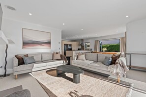 Ein modernes Wohnzimmer mit Sofa, Couchtisch und Blick auf die Küche und den Außenbereich.