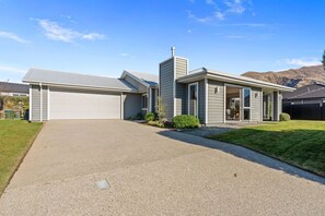 A single-story house with a garage, a covered entryway, and a well-maintained lawn. - Family Ski Base | Boot Dryer | 4Bedroom (Wānaka)