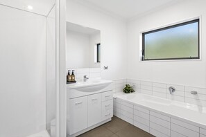 A modern bathroom with a white sink, vanity, and bathtub. - Family Ski Base | Boot Dryer | 4Bedroom (Wānaka)
