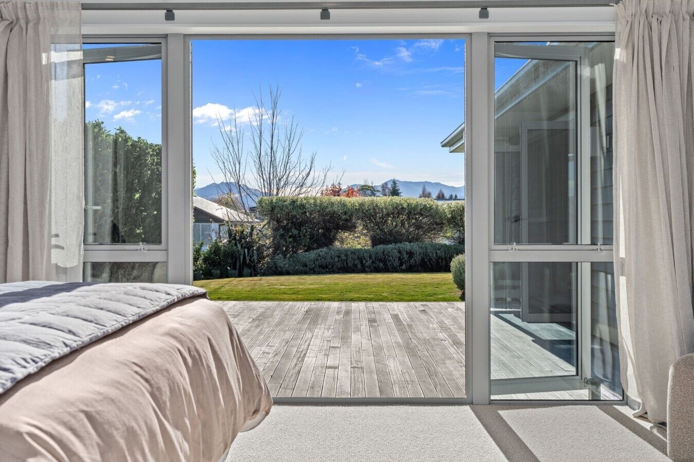 Quarto com uma grande porta de vidro deslizante que dá para um deck de madeira e vista de um jardim paisagístico.
