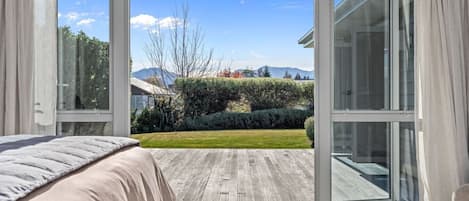 A bedroom with a large sliding glass door leading to a wooden deck and a view of a landscaped garden.