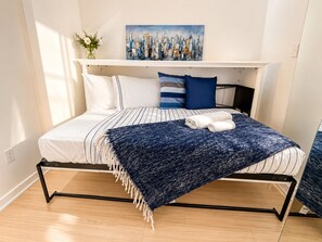A bed with a striped bedspread, a blue throw blanket, and two pillows.