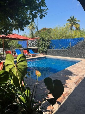 A swimming pool with lounge chairs and a covered seating area.