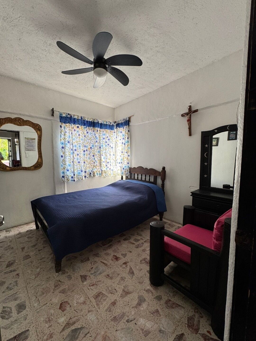 A bedroom with a bed, a dresser, a mirror, a ceiling fan, and a window with curtains.
