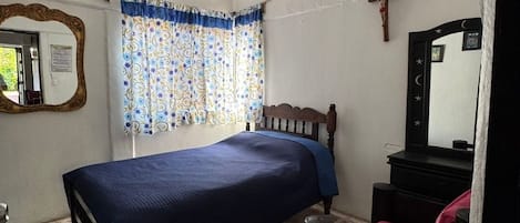 A bedroom with a bed, a dresser, a mirror, a ceiling fan, and a window with curtains.