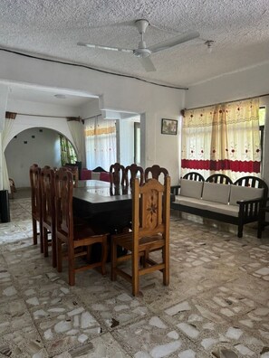 Uma sala de jantar com uma mesa redonda, cadeiras de madeira, um ventilador de teto e um chão com padrão.