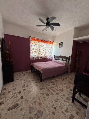 A bedroom with a bed, a ceiling fan, a window with floral curtains, and a tiled floor. - Dianas Home Oaxtepec (México)