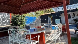 Un espace extérieur aménagé en patio, doté d’un coin salon couvert, d’une piscine et d’un bâtiment à la façade décorative.