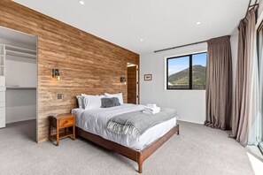 Quarto com parede de destaque em madeira, uma cama grande, mesa de cabeceira, guarda-roupa e janela com vista para colinas.