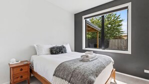Ein Schlafzimmer mit einem Bett, einem Nachttisch, einem Fenster mit Blick ins Freie und einer grauen Wand.