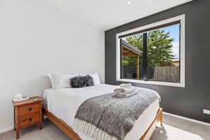 A bedroom with a bed, a nightstand, a window with a view of the outdoors, and a grey wall. - Luxury Hāwea | Alfresco Retreat | Sleeps 6 (Lake Hāwea)