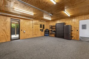 A room with wooden walls and ceiling, a grey carpet, a black refrigerator, and a black cabinet.