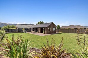 A modern house with a large backyard, a wooden deck, and a fenced area.