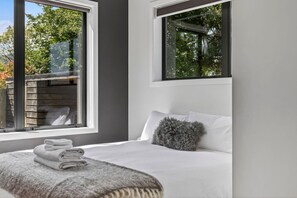 A modern bedroom with a bed, a window, and a view of trees.
