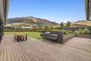 A deck with a barbecue area, a table, and a view of a hilly landscape.