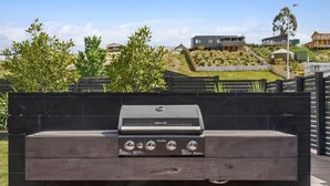 Ein Grill im Freien mit Bedienfeld vor einer Gartenlandschaft und Wohnhäusern.