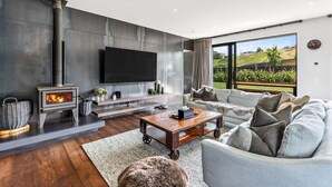 Ein modernes Wohnzimmer mit Kamin, Flachbildfernseher, Sofa und großem Fenster mit Blick ins Freie.