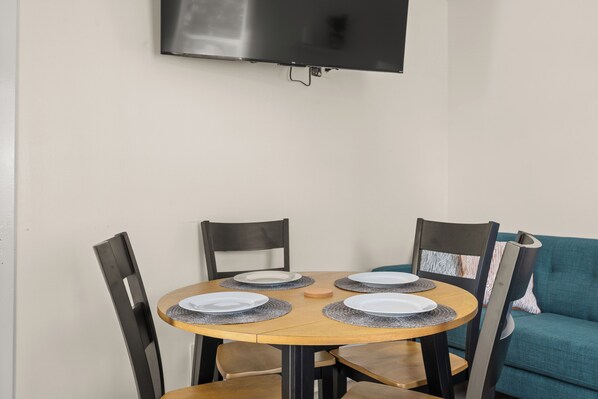 A dining area with a round table, four chairs, and a flat-screen TV mounted on the wall.