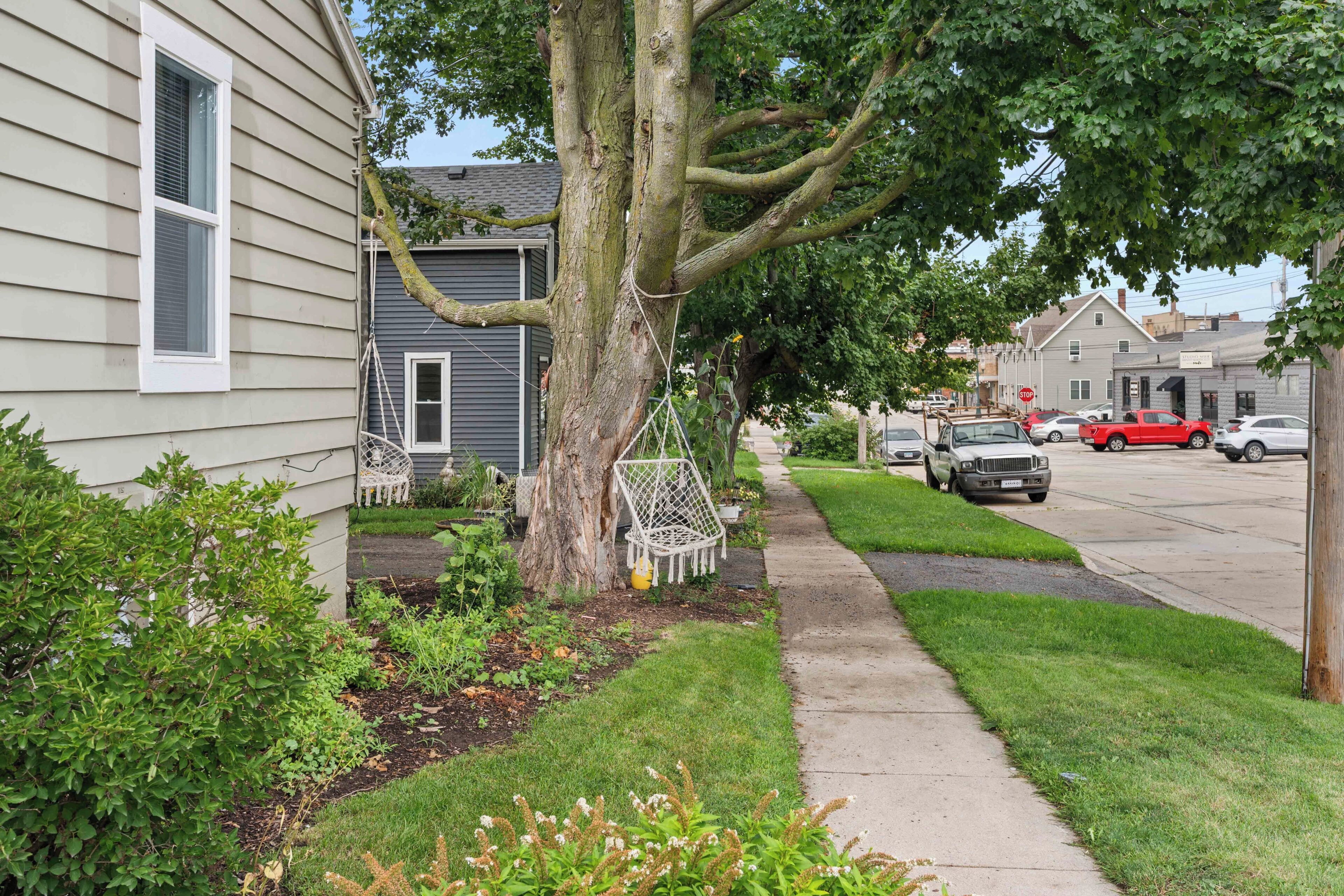 Une rue résidentielle bordée de maisons, avec un trottoir et des voitures garées.