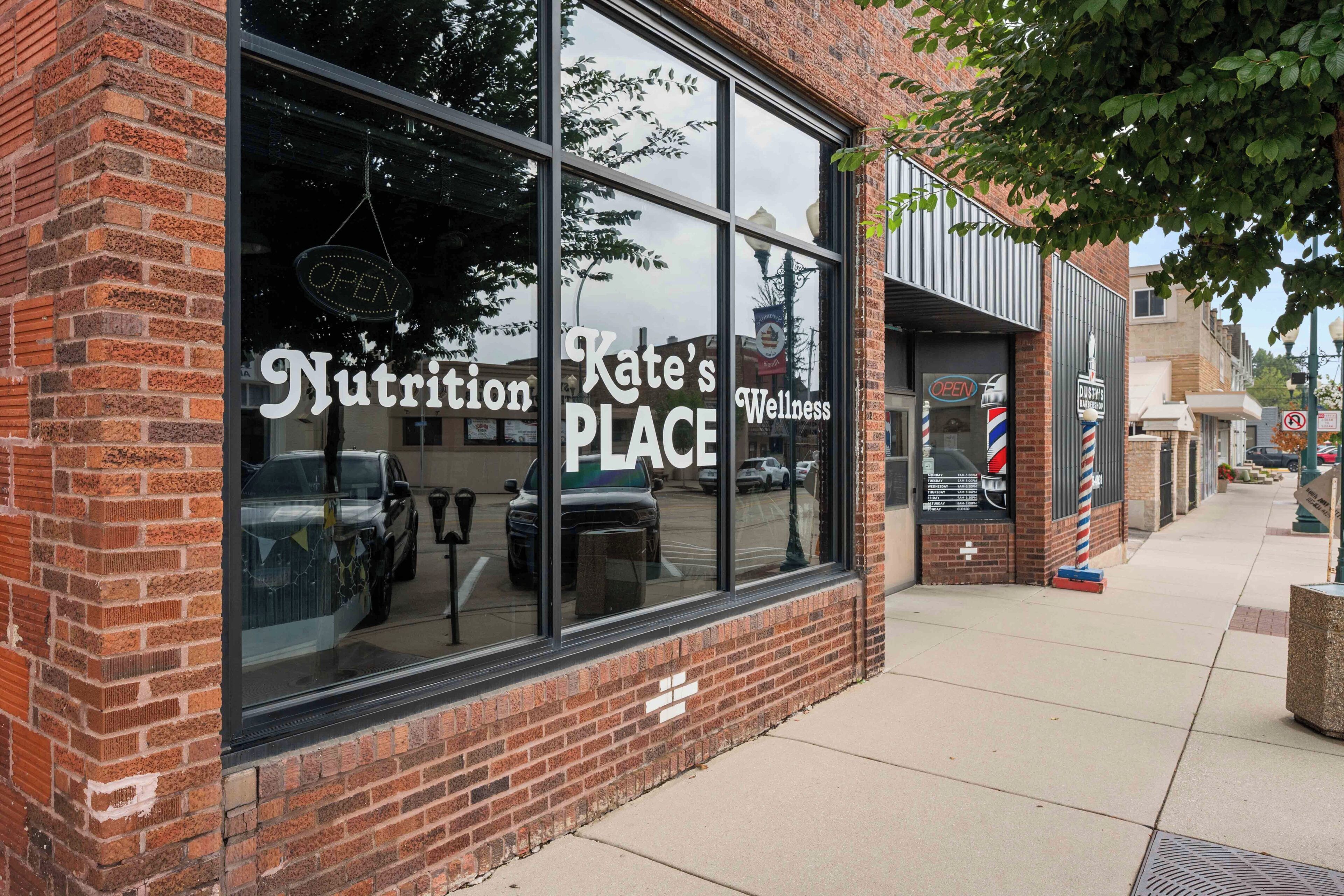 Un edificio de ladrillo con amplias ventanas que muestran los rótulos 'Kate's Wellness' y 'Nutrition Place'.