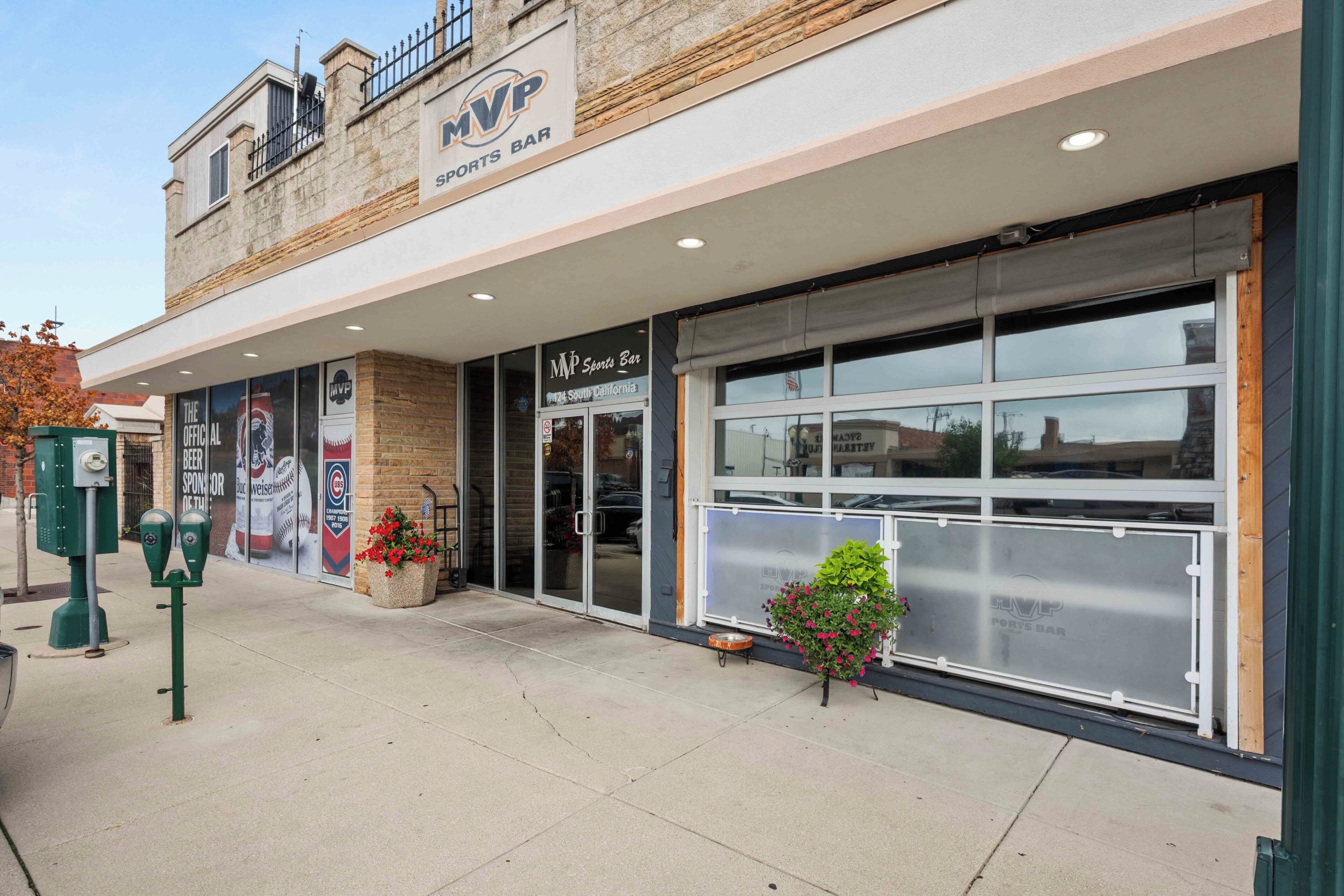 A sports bar with a large glass storefront, outdoor seating, and a brick facade.