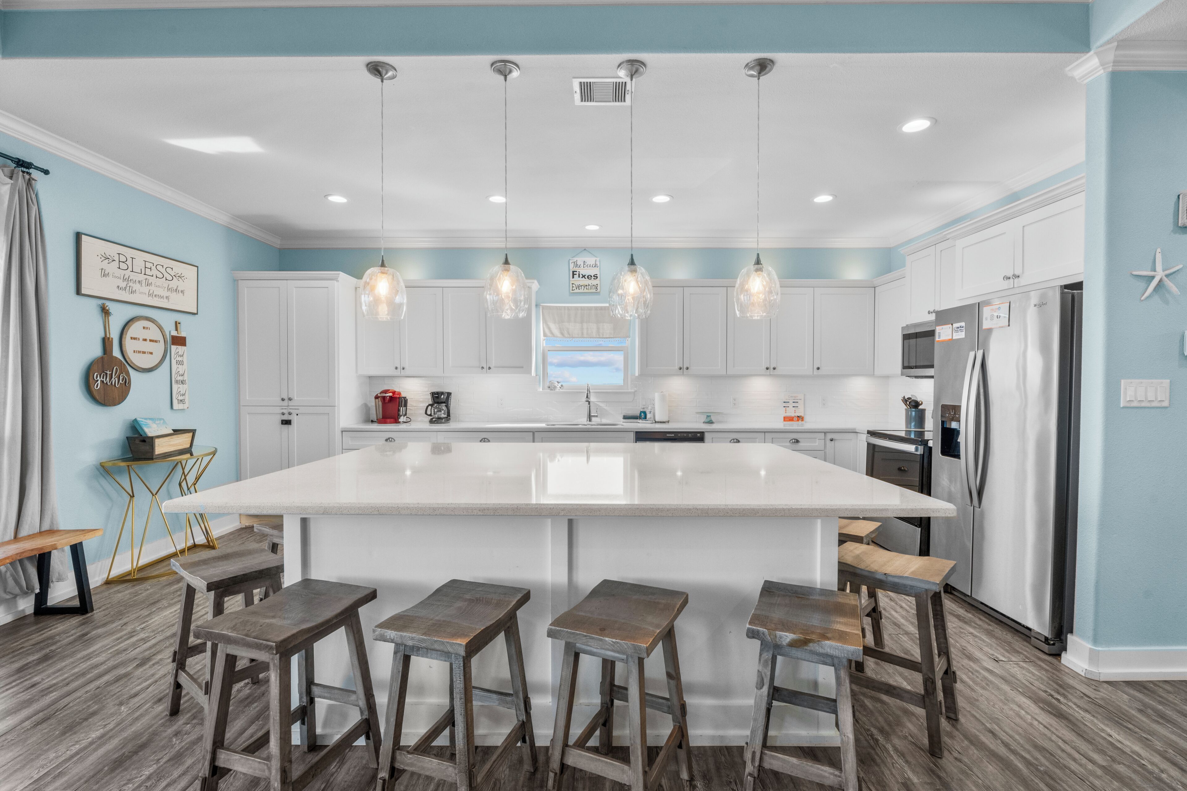 A kitchen with a central island, bar stools, white cabinets, stainless steel appliances, and pendant lighting.