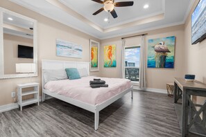 A bedroom with a bed, a ceiling fan, artwork on the walls, and a view through the window. - Beachfront Home in Crystal Beach | Private Hot Tub | Double Decks | Outdoor Bar | Sleeps 16 (Crystal Beach)