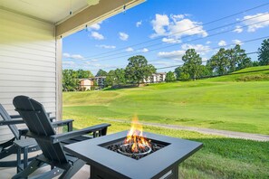 Eine Terrasse mit Sitzgelegenheiten im Freien und einem Feuerbereich mit Blick auf einen gepflegten Rasen und Wohnhäuser.