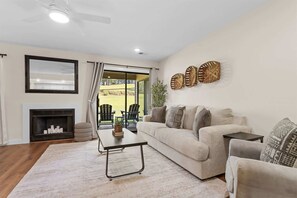 Un salon avec une cheminée, un canapé, une table basse et une vue sur un patio aménagé avec des sièges d’extérieur.