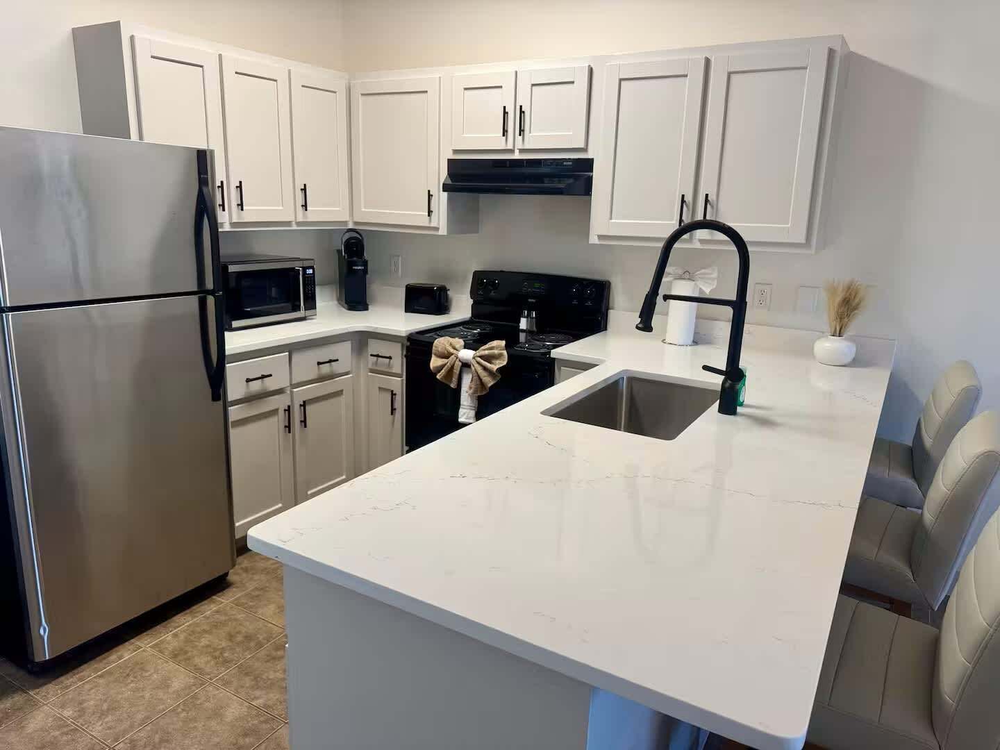 A modern kitchen with white cabinetry, stainless steel appliances, and a marble countertop.