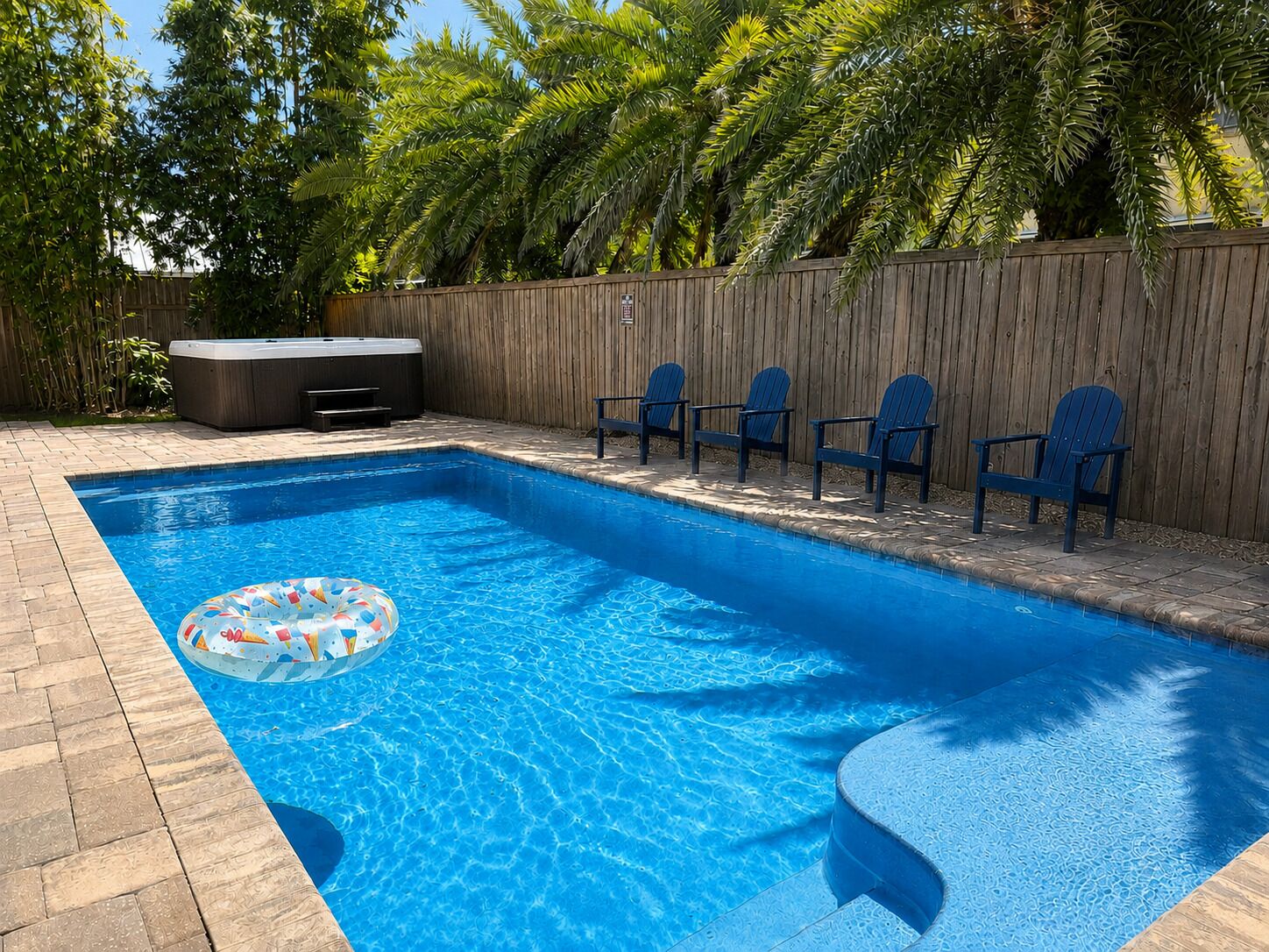 Une piscine rectangulaire dotée d’un jacuzzi et de chaises longues disposées le long du bord.