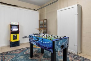 Una habitación con mesa de futbolín, consola de videojuegos y estantería.