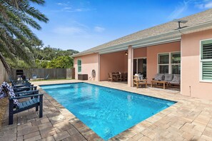 Una piscina con zona de patio, mobiliario exterior y un área de estar cubierta.