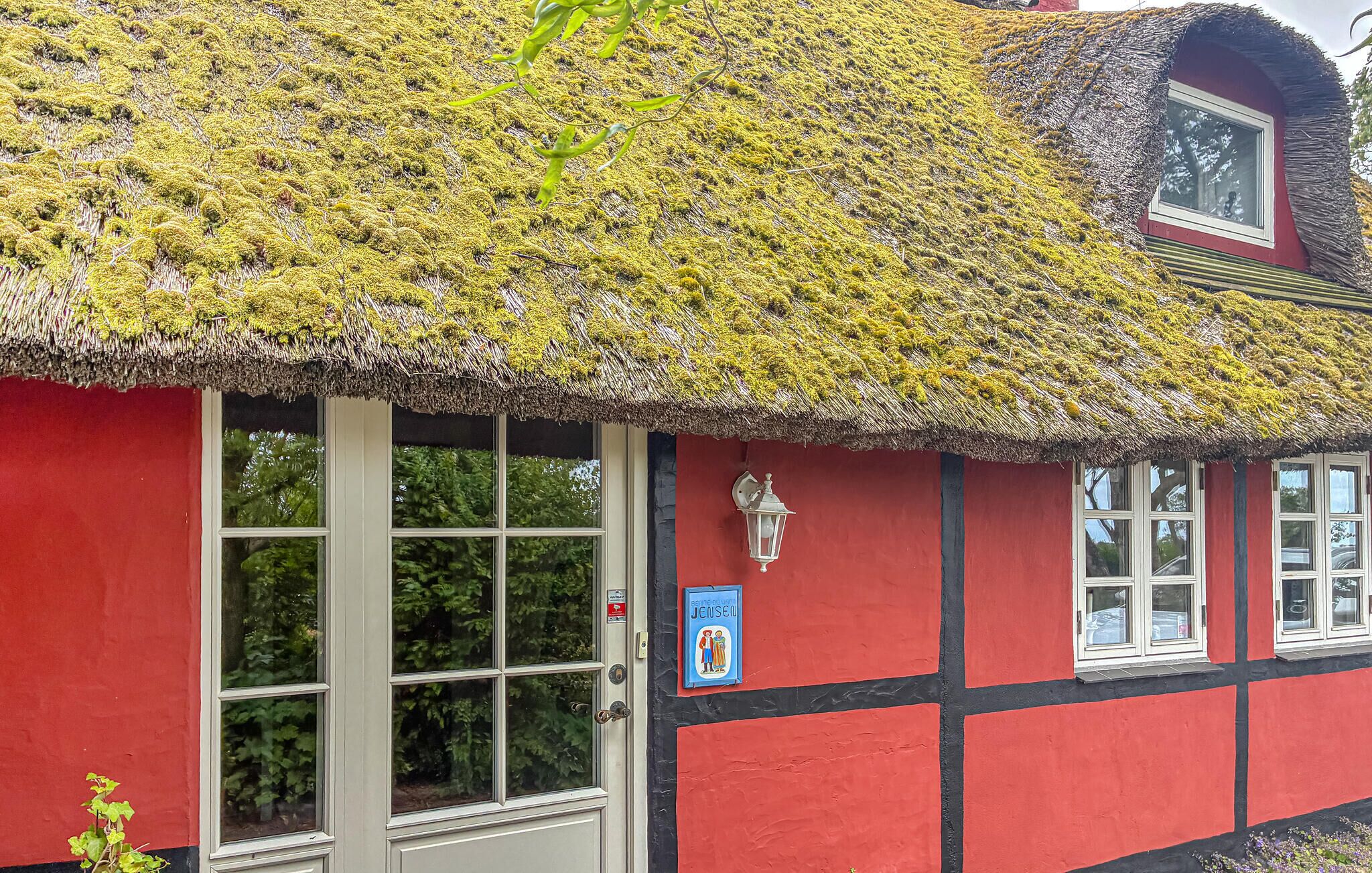 Een klassiek gebouw met een met mos begroeid rieten dak, een rode gevel en een klein raam met een bord.