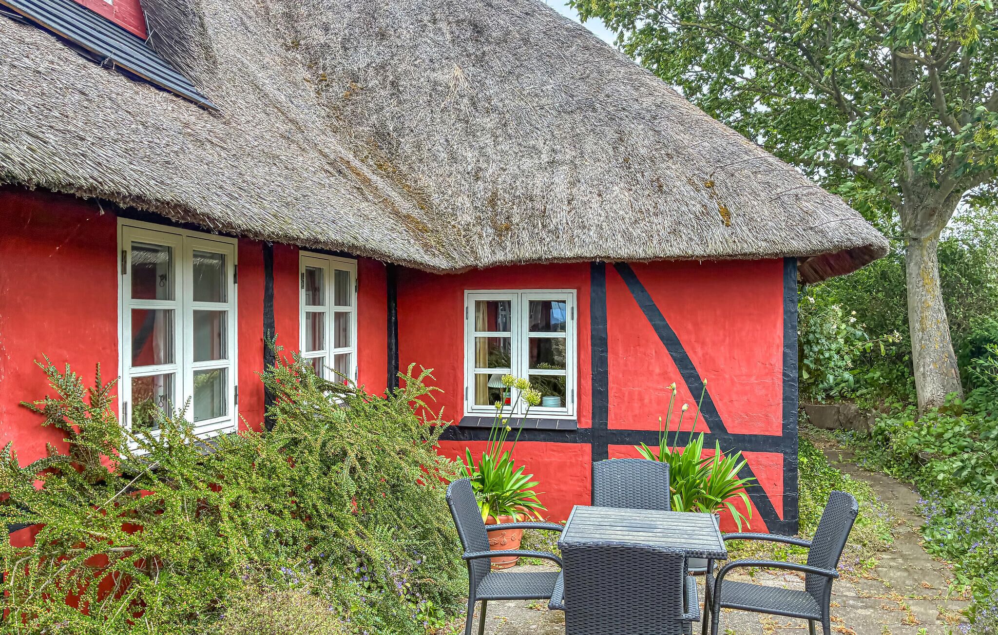 A red house with a thatched roof, white windows, and a black and red striped wall.