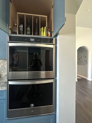 Une cuisine équipée de deux fours en acier inoxydable, d’un meuble à vin intégré et d’une personne se tenant dans l’embrasure de la porte.