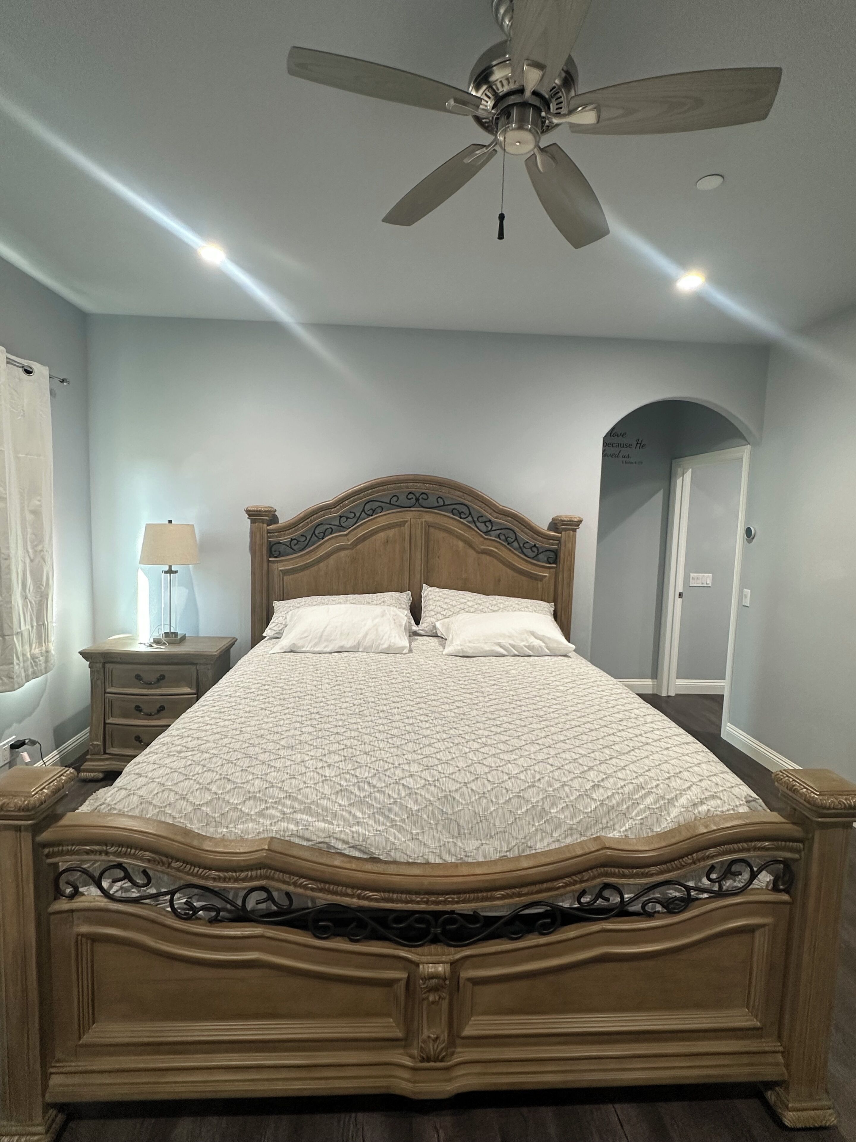 A bedroom with a wooden bed, a nightstand, a lamp, and a ceiling fan.
