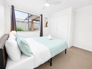 A bedroom with a bed, a nightstand, a window with curtains, a ceiling fan, and a door.